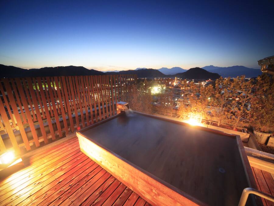 A wooden deck with a hot tub, surrounded by a wooden fence, overlooking a cityscape with mountains in the background.