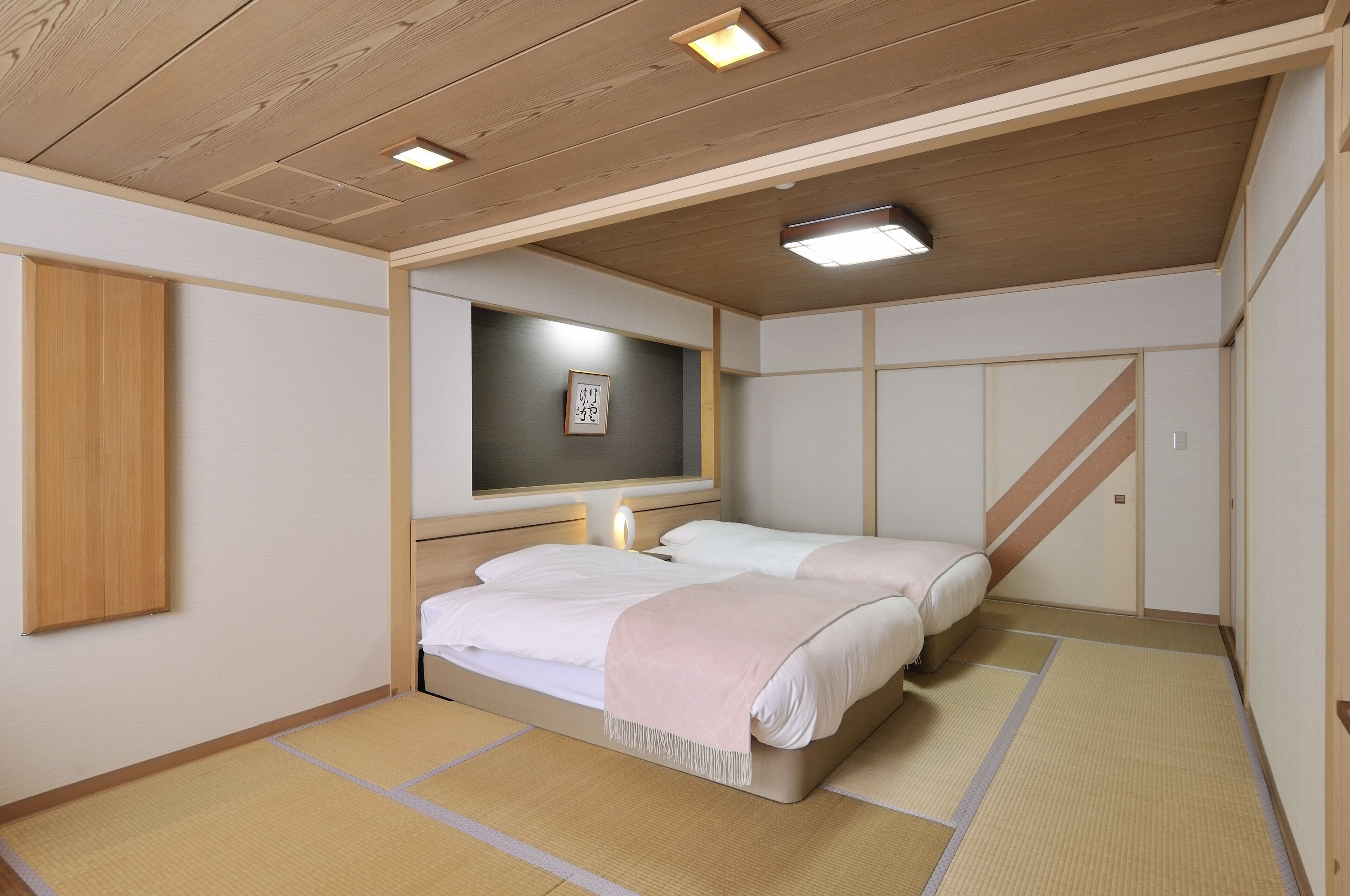 Un dormitori tradicional japonès amb sòl de tatami, un llit amb roba de llit blanca, un armari de fusta i una televisió penjada a la paret.