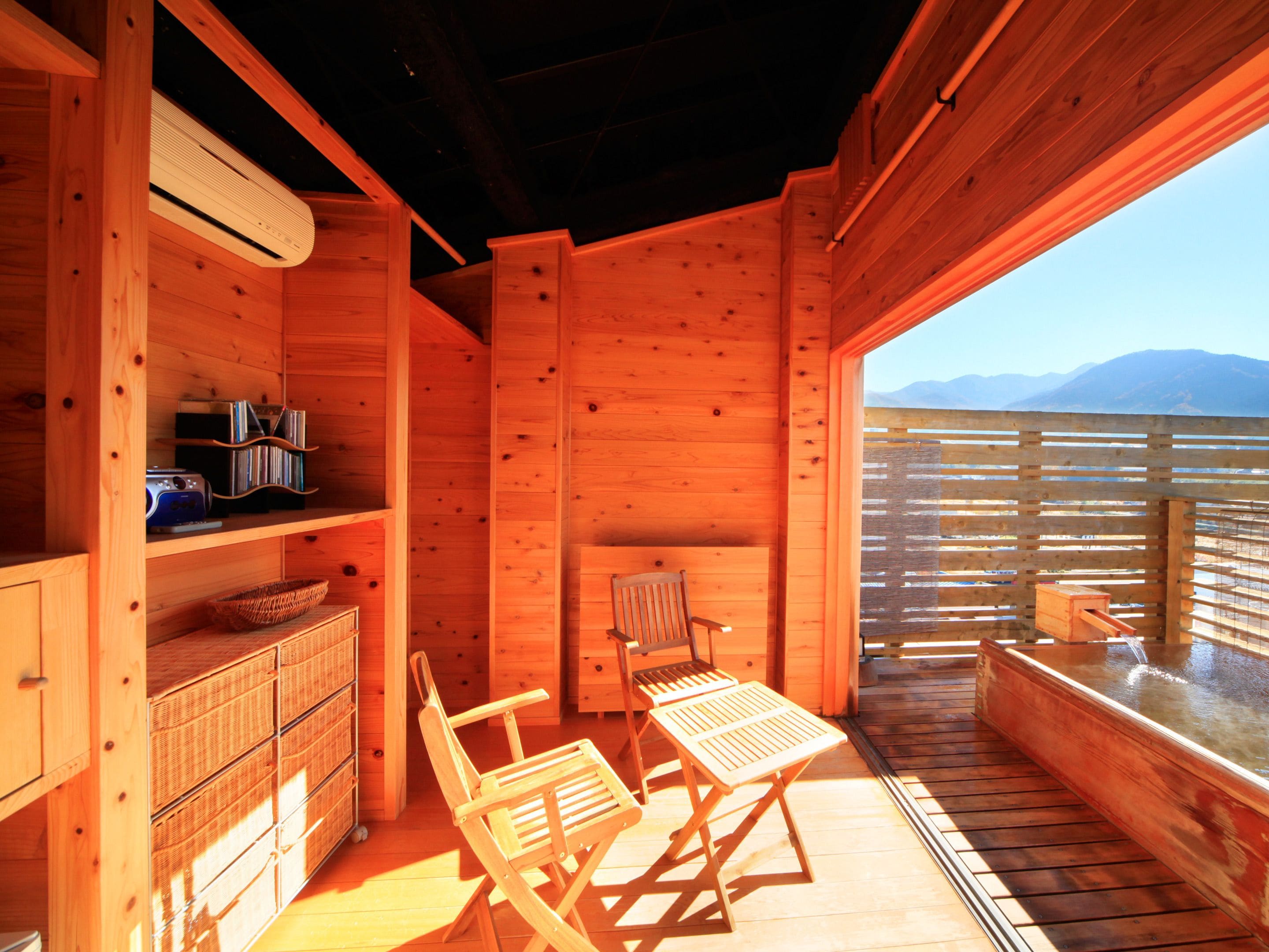 Una baita in legno con un balcone, un tavolo e sedie, un caminetto e vista sulle montagne.