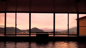 A room with large windows offering a view of a mountainous landscape during sunset.