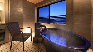A modern bathroom with a freestanding bathtub, a chair, and a window with a view of the ocean.