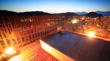Um deck de madeira com uma banheira de hidromassagem, com vista para o horizonte urbano ao entardecer.