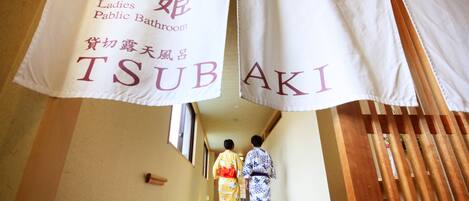 A traditional Japanese interior with a wooden staircase and two individuals in kimonos.