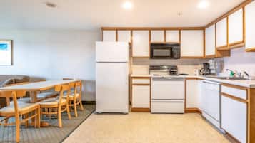 Cocina compacta con refrigerador, microondas, estufa y lavavajillas. Cuenta con una mesa de comedor con sillas y una pequeña zona de estar con un sofá.