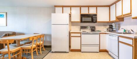 A compact kitchen with a refrigerator, microwave, stove, and dishwasher. There is a dining table with chairs and a small seating area with a couch.