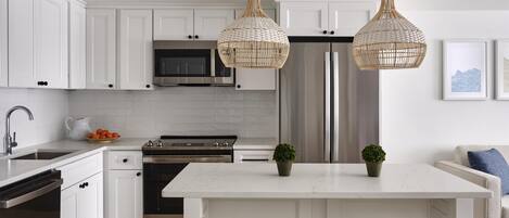 A modern kitchen with white cabinetry, stainless steel appliances, a central island with chairs, and hanging wicker pendant lights.