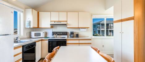 A modern kitchen with white cabinets, a microwave, stove, and a dining table with chairs.