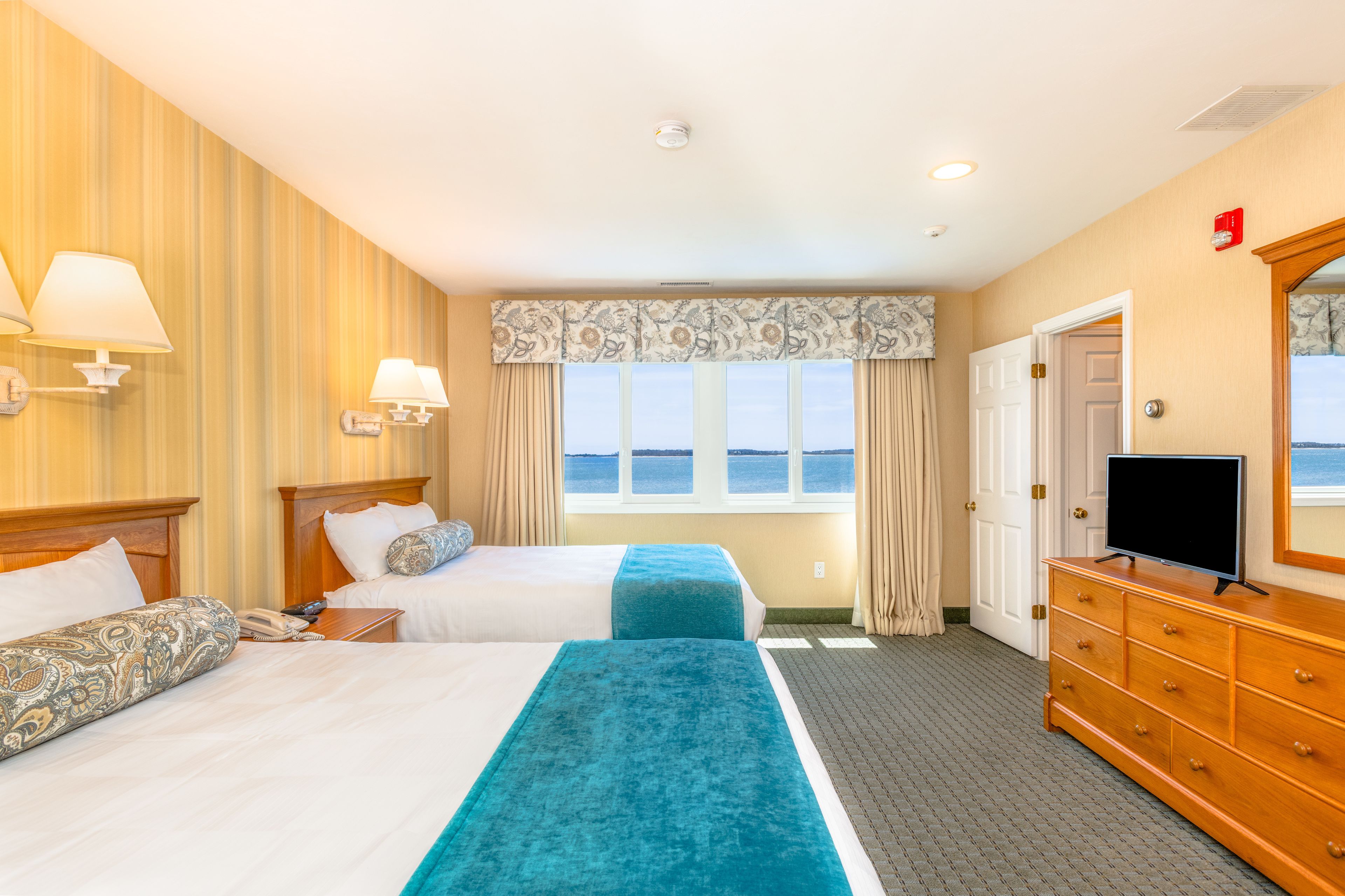 Une chambre d’hôtel avec deux lits, un téléviseur posé sur une commode et une fenêtre donnant sur la mer.