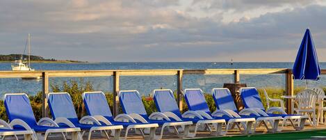Un espace aménagé au bord de la piscine, avec des chaises longues et des parasols, offrant une vue sur une étendue d’eau et une île lointaine.