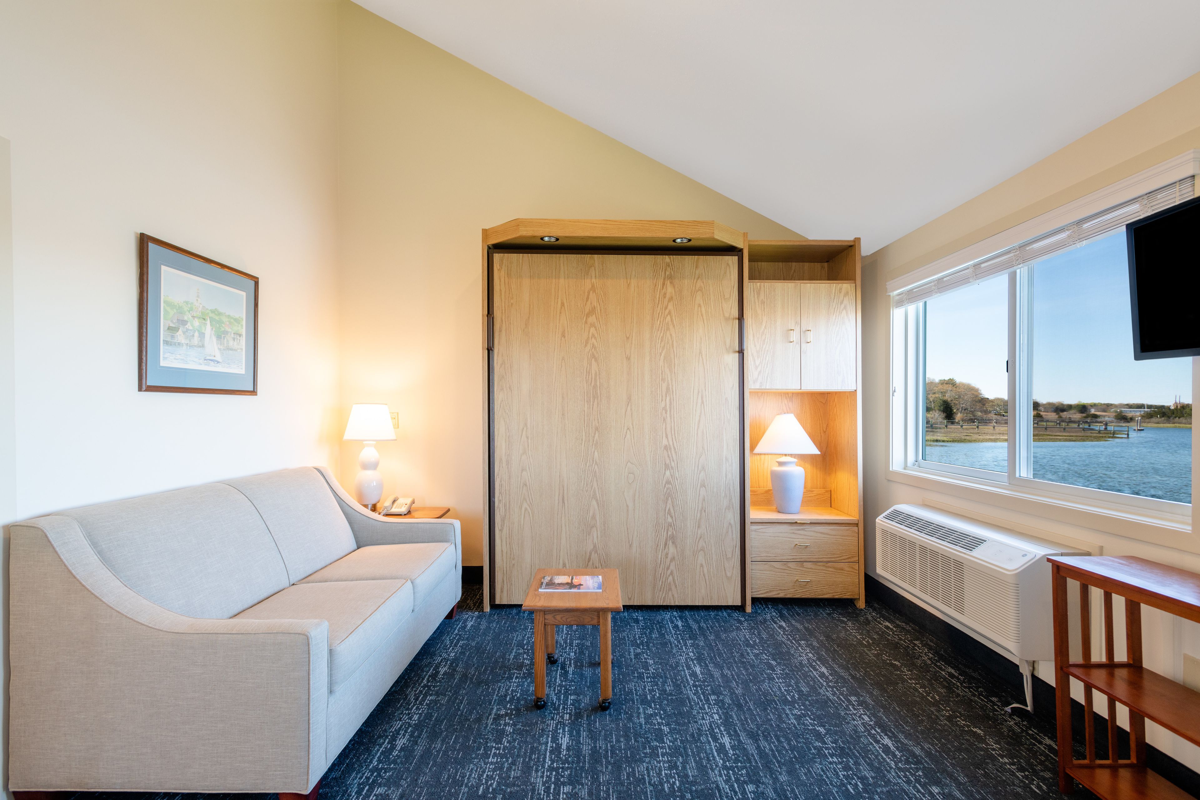 Et hotelværelse med en sofa, et lille bord, et træskab, et fjernsyn og et vindue med udsigt over vandet.