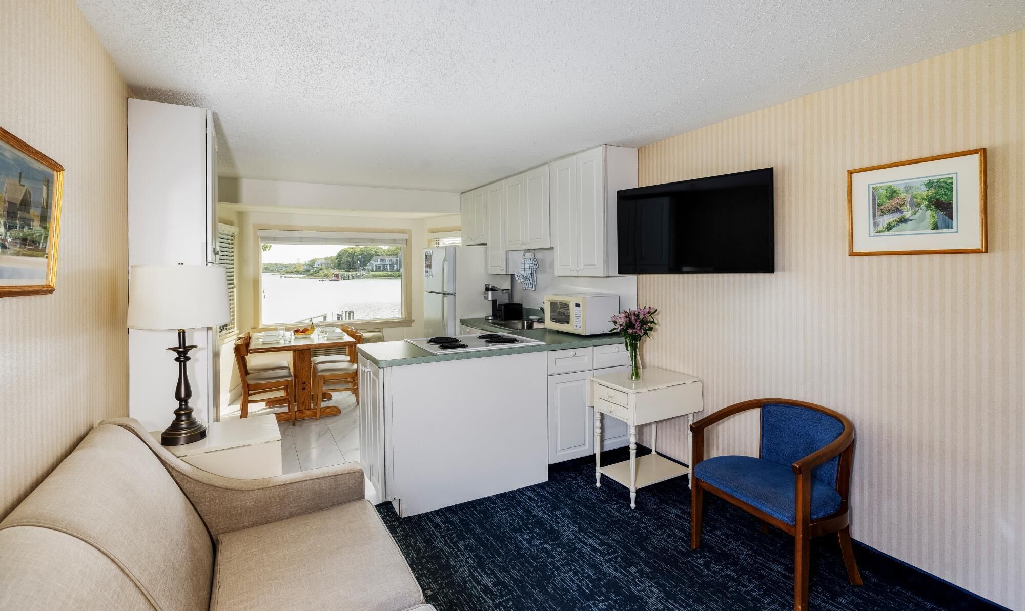 A compact kitchen with a dining area, a flat-screen TV mounted on the wall, and a small seating area with a chair.