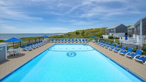 Ein Schwimmbecken mit Liegestühlen und Sonnenschirmen, umzäunt mit Blick aufs Meer.