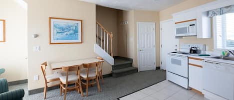 A kitchen with white appliances, a dining area with wooden chairs, and a staircase leading to another level.