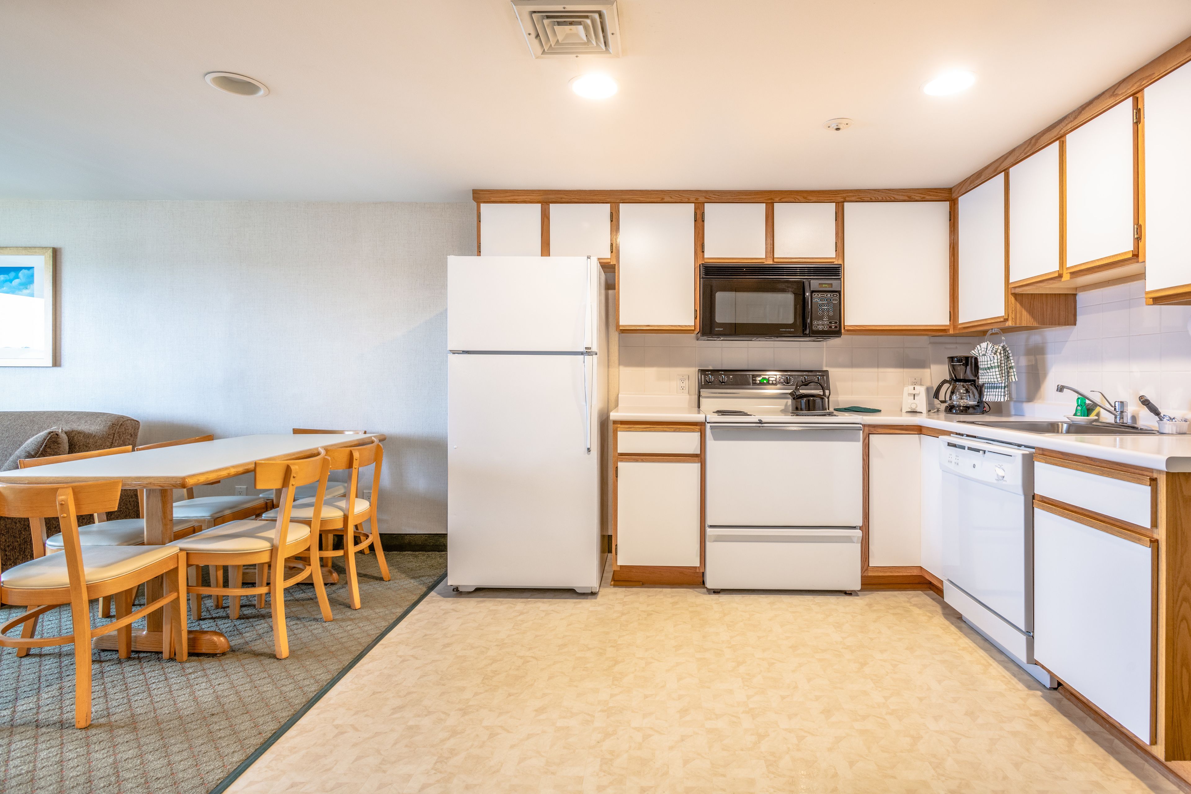 A compact kitchen with a refrigerator, microwave, stove, and dishwasher. There is a dining table with chairs and a small seating area with a couch.