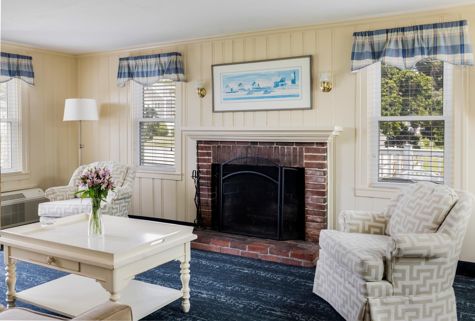 Una sala de estar acogedora con chimenea, sillones estampados, una mesa de centro con un jarrón de flores y un cuadro en la pared.