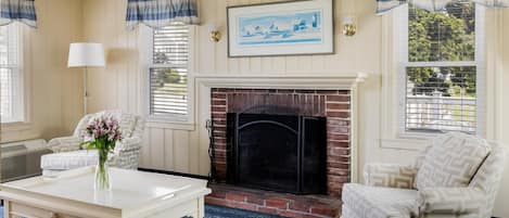 Una sala de estar acogedora con chimenea, sillones estampados, una mesa de centro con un jarrón de flores y un cuadro en la pared.