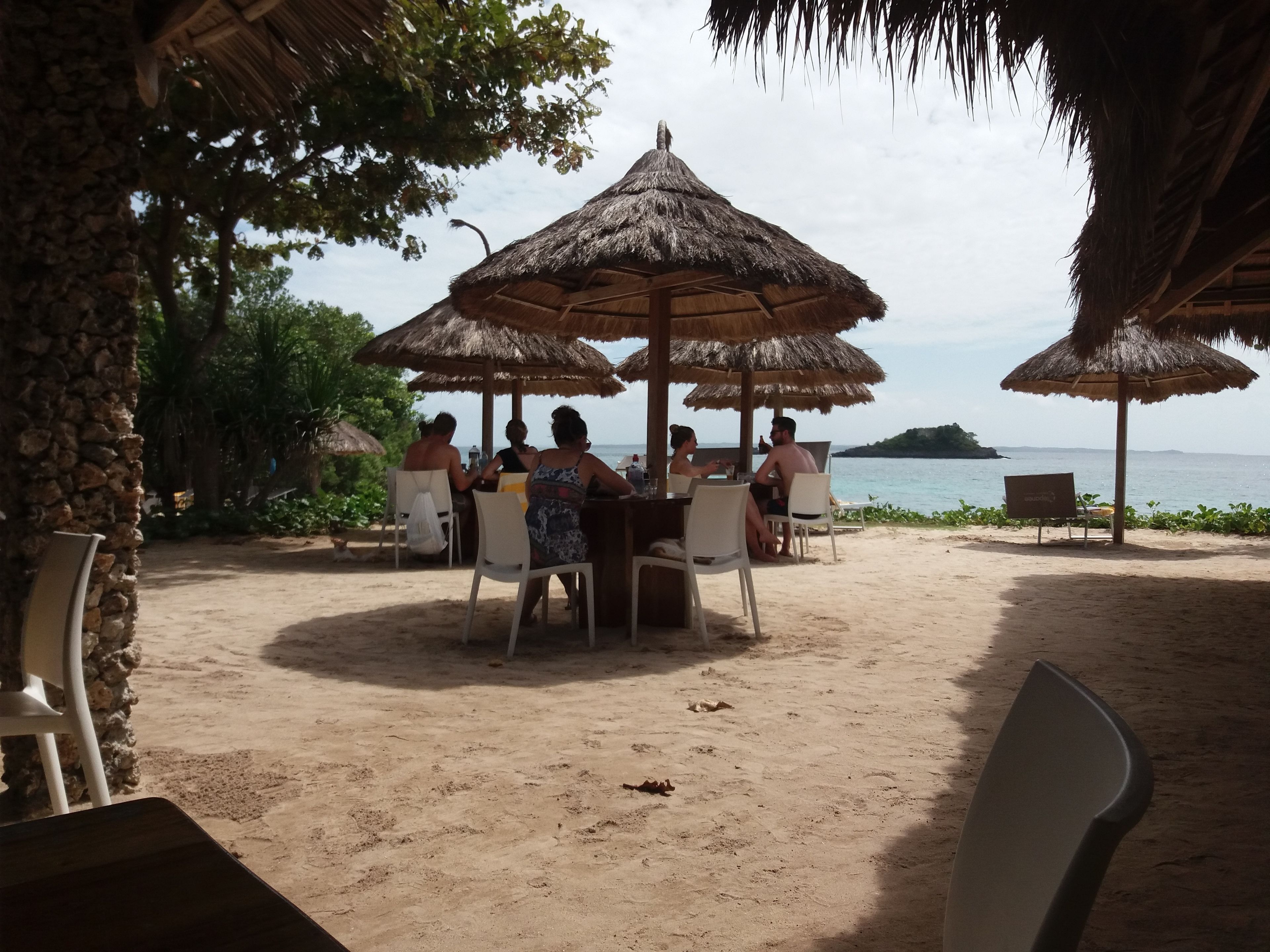 A beachside dining area with thatched umbrellas, white chairs, and a view of the sea.