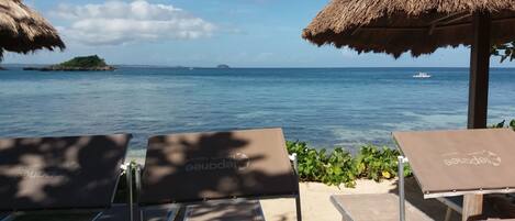 A beachside lounge with thatched umbrellas and lounge chairs facing the ocean.