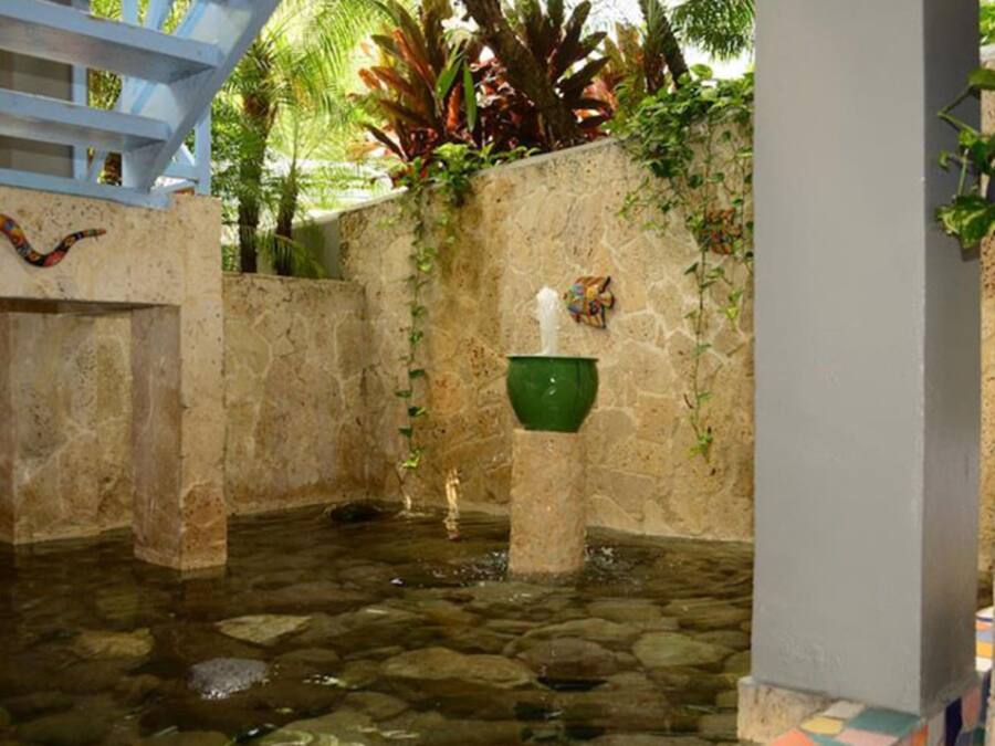 Un patio con paredes de piedra, una fuente de agua, un jarrón verde y una escalera azul.