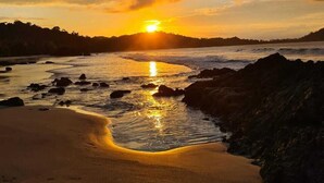A sunset over a beach with rocks and sand. - Hotel Plaza Yara (Quepos)