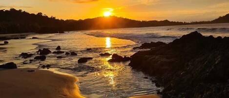 Un atardecer sobre una playa con rocas y arena.
