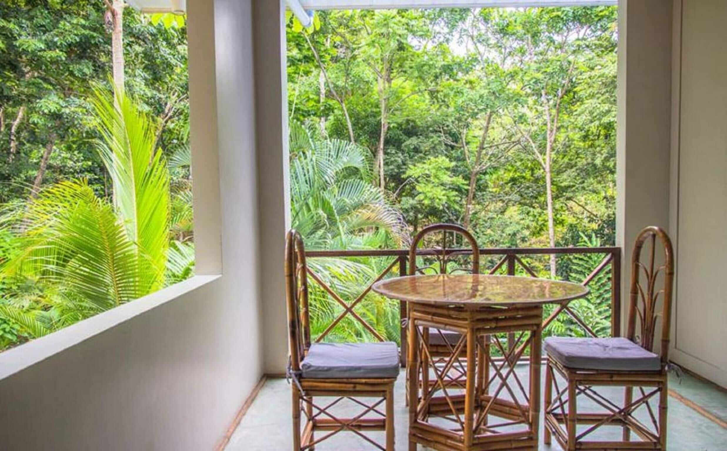 A balcony with a round table and four chairs, overlooking a lush green forest.