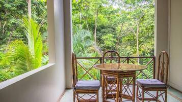 A balcony with a round table and four chairs, overlooking a lush green forest.