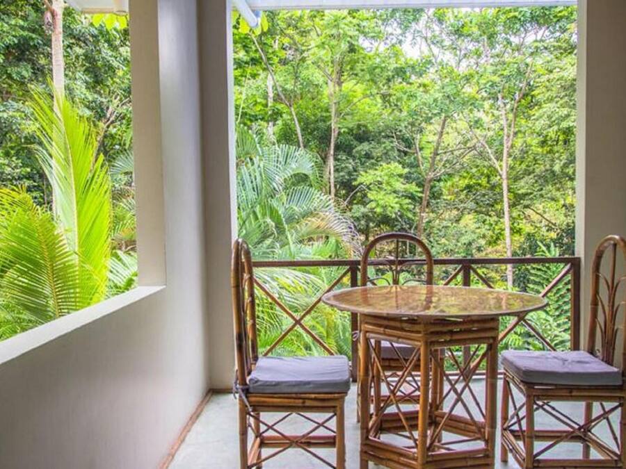 A balcony with a round table and four chairs, overlooking a lush green forest.
