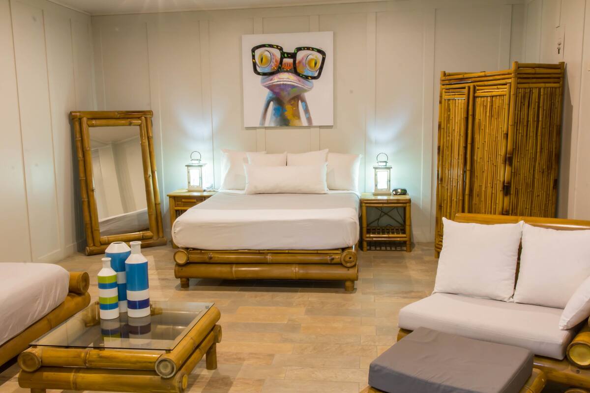 A room with a bed, a sofa, a glass-top table, and a mirror.