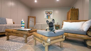 A cozy living room with a French Bulldog on a cushioned stool, a sofa, a coffee table, and a painting on the wall.