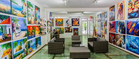 An art gallery with various paintings on the walls, wicker furniture, and a green floor.