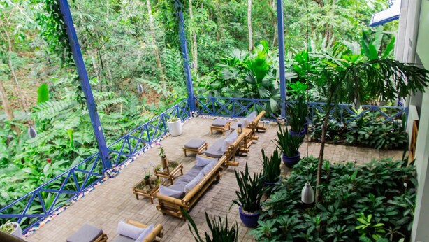 A covered outdoor lounge area with wooden lounge chairs and potted plants. - Hotel Plaza Yara (Quepos)
