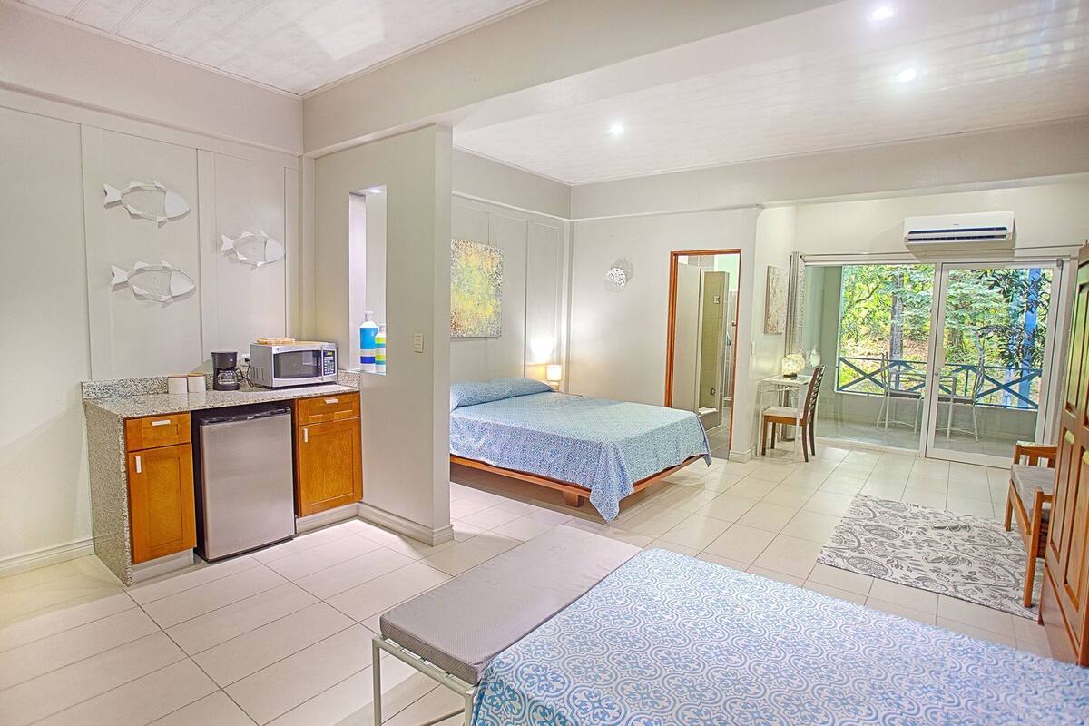 A hotel room with a kitchenette, a bed, a small table, and a view of the outdoors.