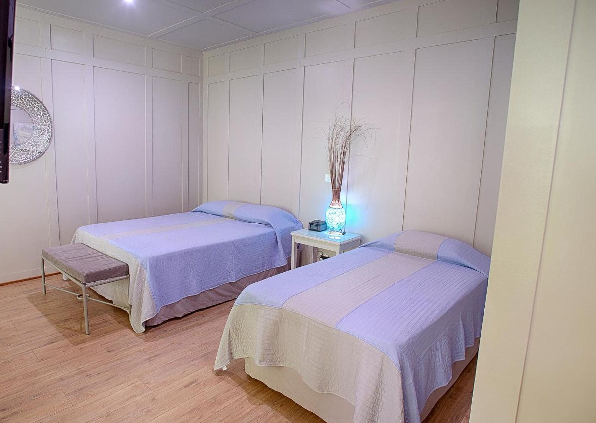 A room with two single beds, a bedside table with a lamp, and a wall-mounted decorative item.