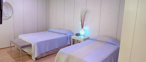 A room with two single beds, a bedside table with a lamp, and a wall-mounted decorative item.