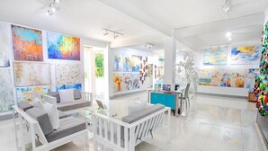 A modern art gallery with white furniture, including sofas and a glass table, and a variety of colorful paintings on the walls. - Hotel Plaza Yara (Quepos)