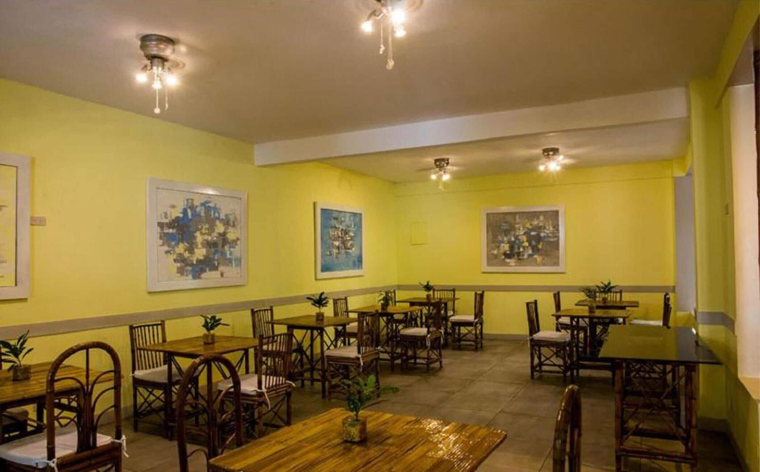 Comedor con varias mesas y sillas, paredes amarillas y luces en el techo.