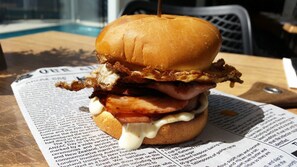 En burger med bacon, ost og sauce i en bolle, placeret på en avis.
