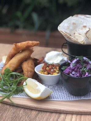 A wooden table with a meal consisting of fried fish, a bowl of salad, a bowl of sauce, a slice of lemon, and a piece of flatbread. - ibis Styles Broken Hill (Broken Hill)