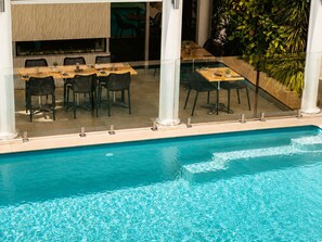 Un área junto a la piscina con comedor y vistas al estanque.