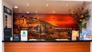 Een receptiebalie met een panoramisch muurschildering, een bord met prioritaire verwelkoming en een bedieningsknop.