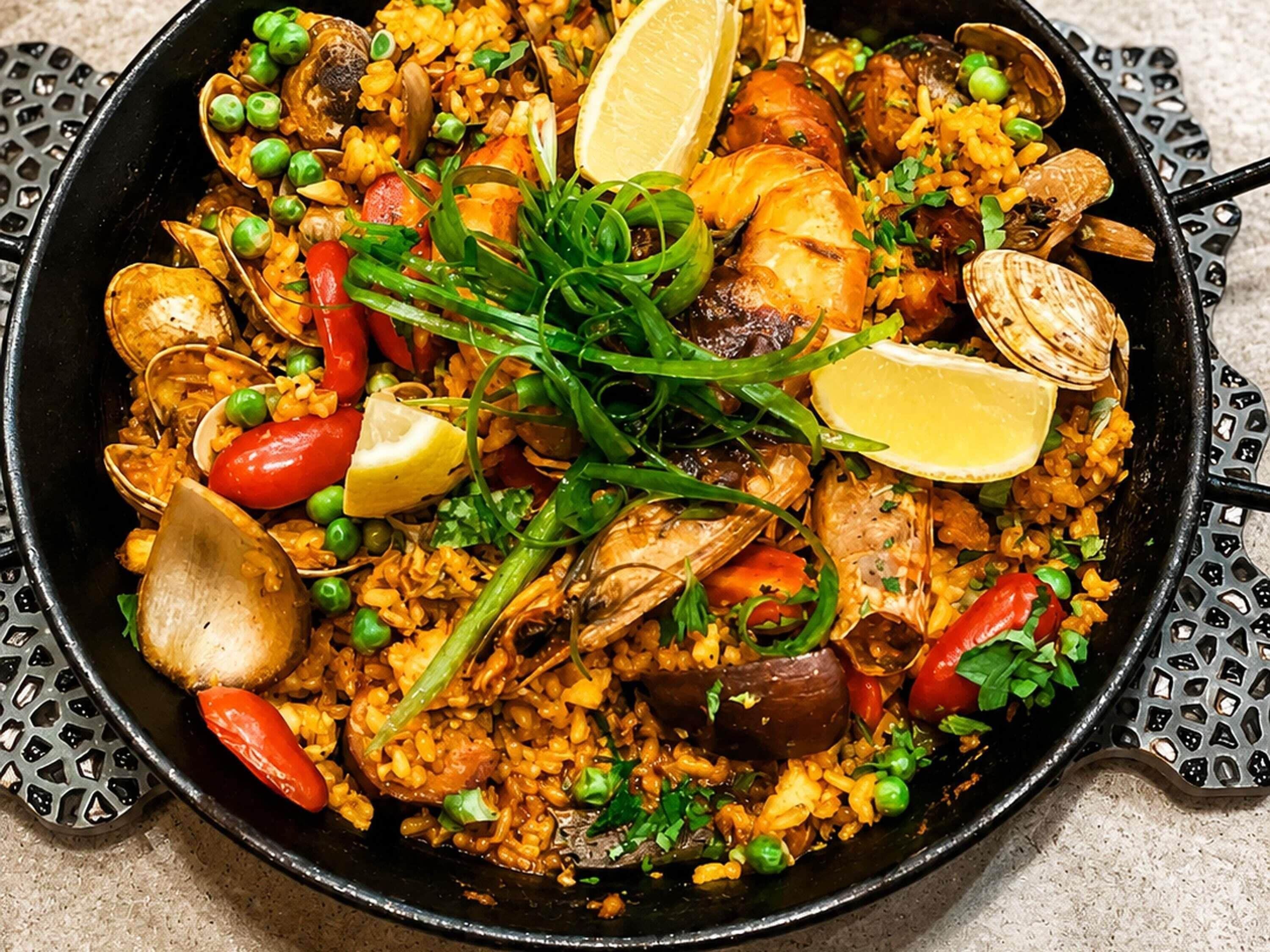 En stor, sort pande fyldt med et farverigt seafood- og risret, pyntet med citronskiver og grønne krydderurter.