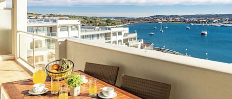 A balcony with a wooden table set for breakfast, overlooking a marina with boats.
