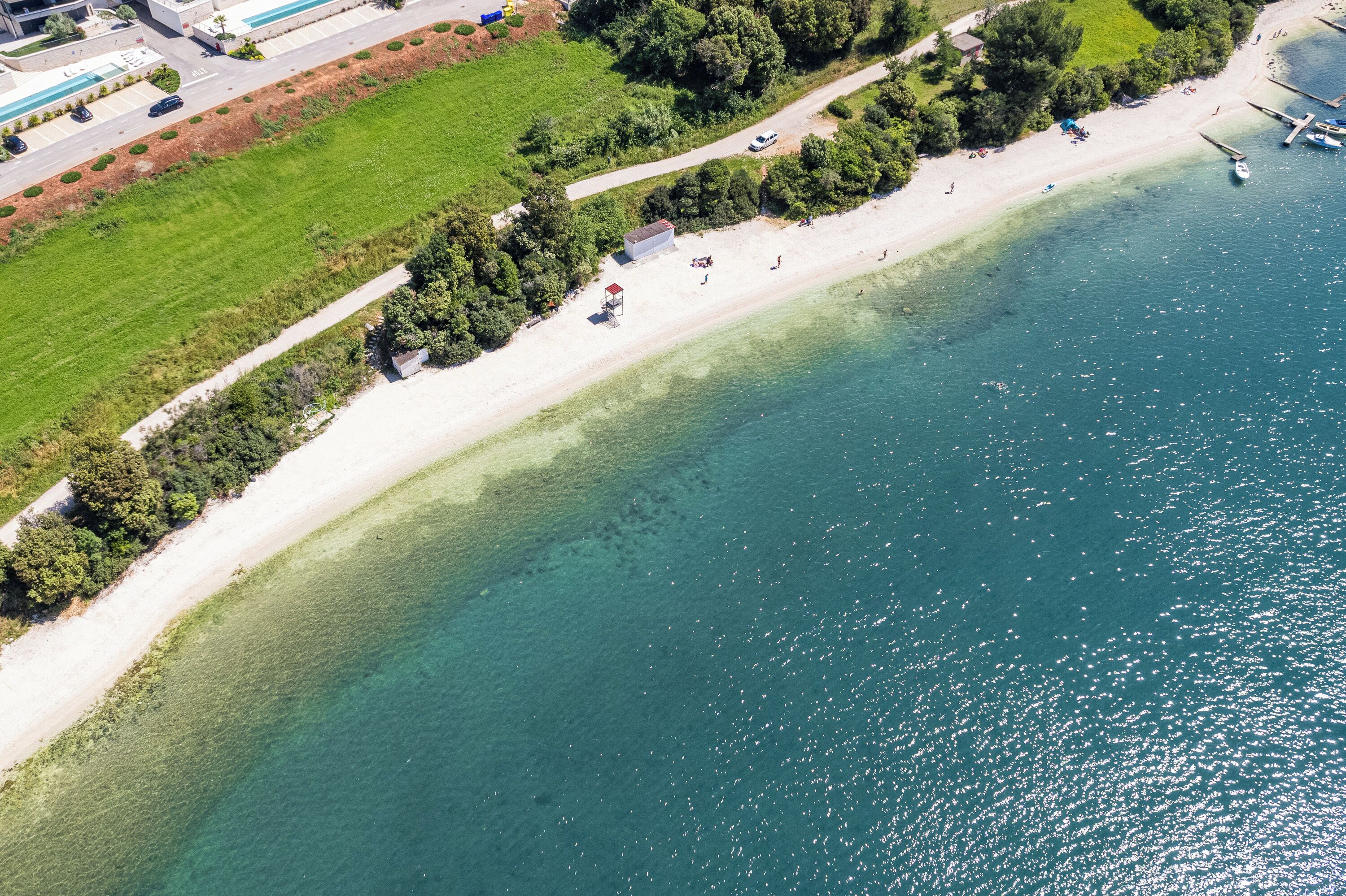 An aerial view of a beach with a clear path, a small structure, and a boat dock.