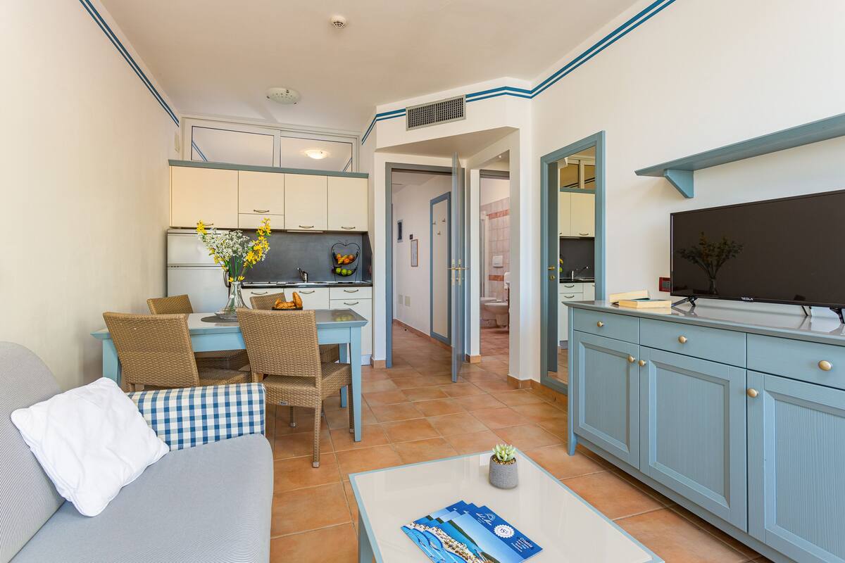 Un espacio habitable compacto con comedor, kitchenette y televisor sobre un mueble.
