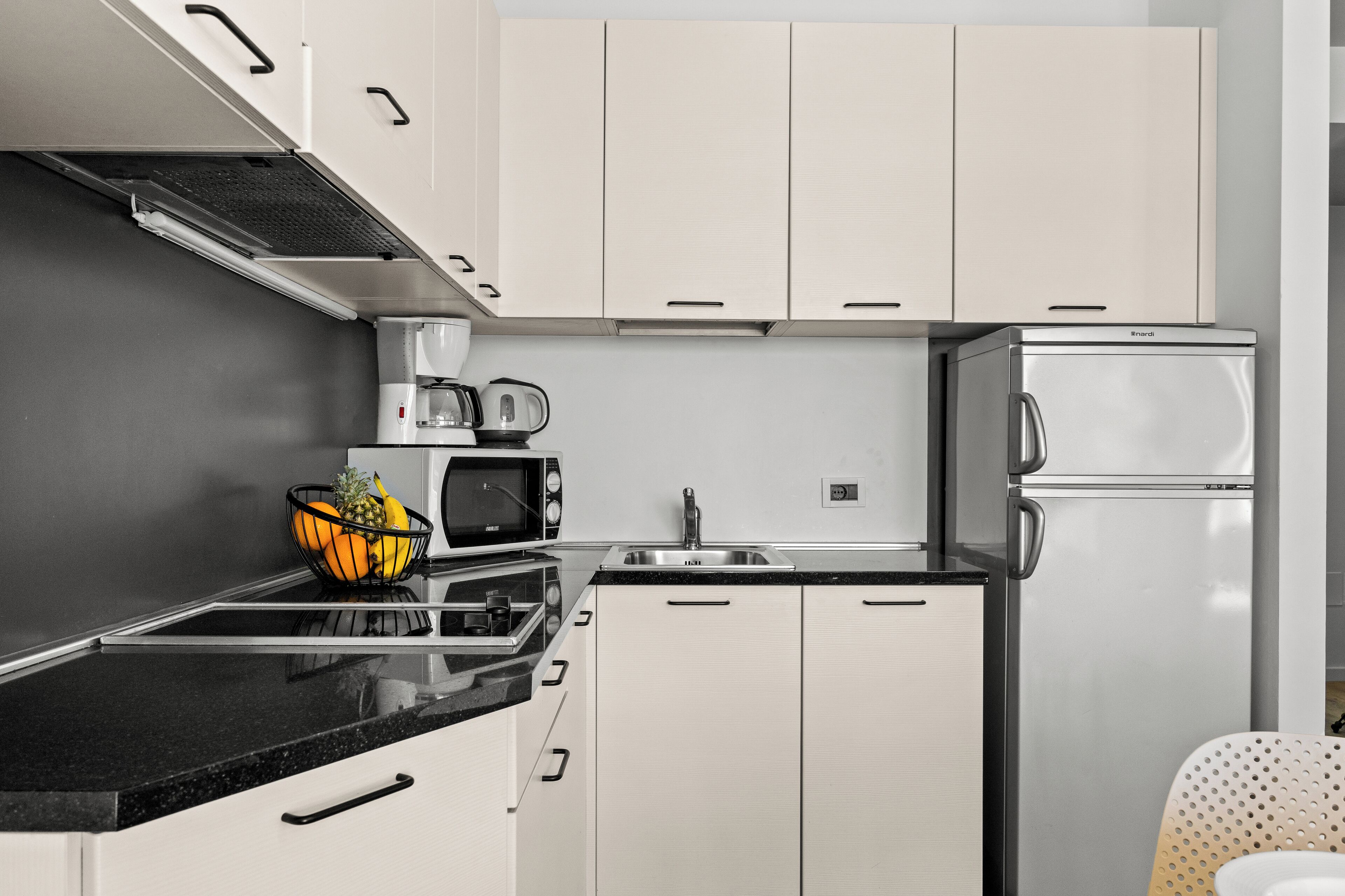 A modern kitchen with white cabinets, a black countertop, a stainless steel refrigerator, a microwave, a toaster, and a sink.