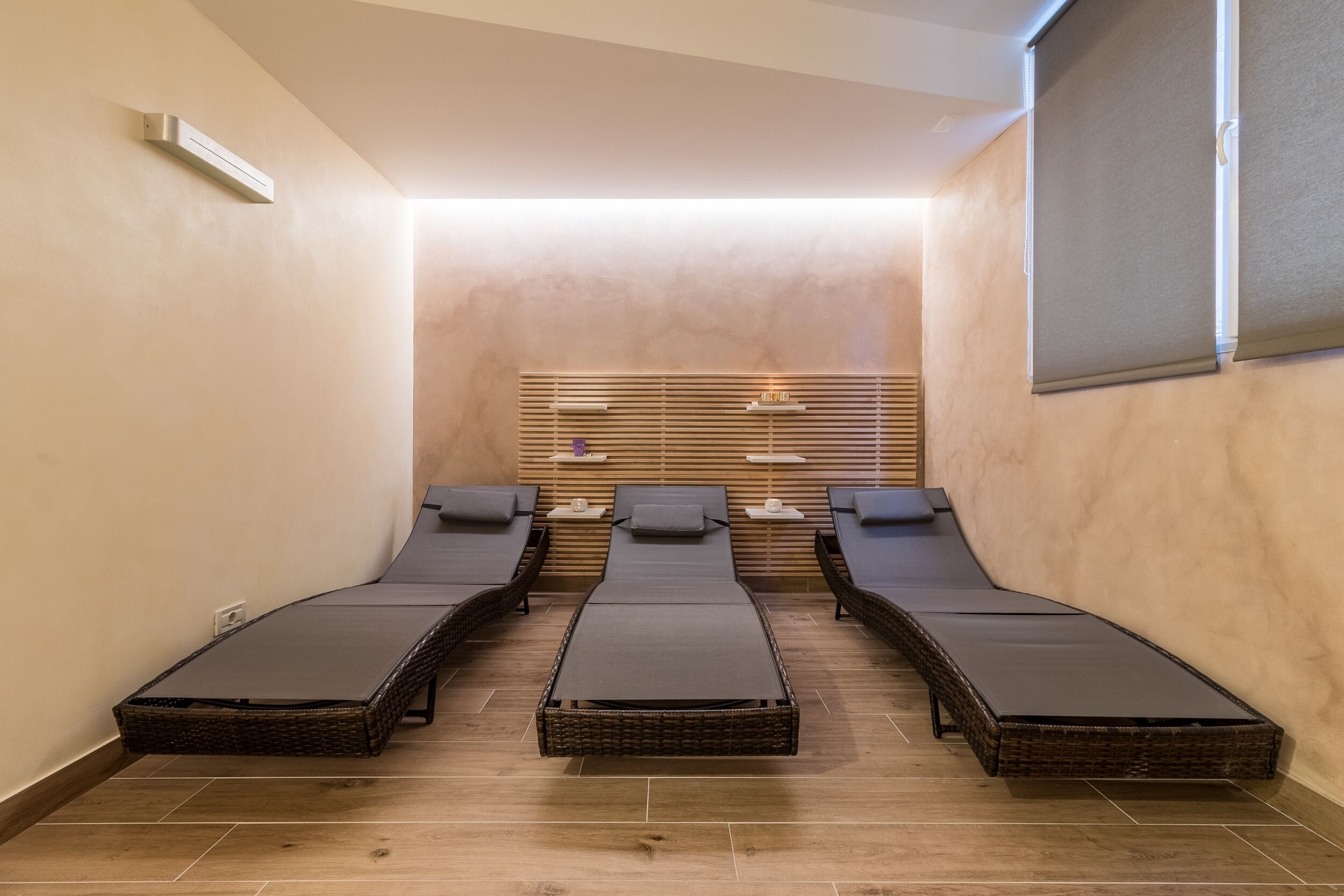 Un cuarto de spa con tres sillones reclinables, un muro de listones de madera y una mesita con una lámpara.