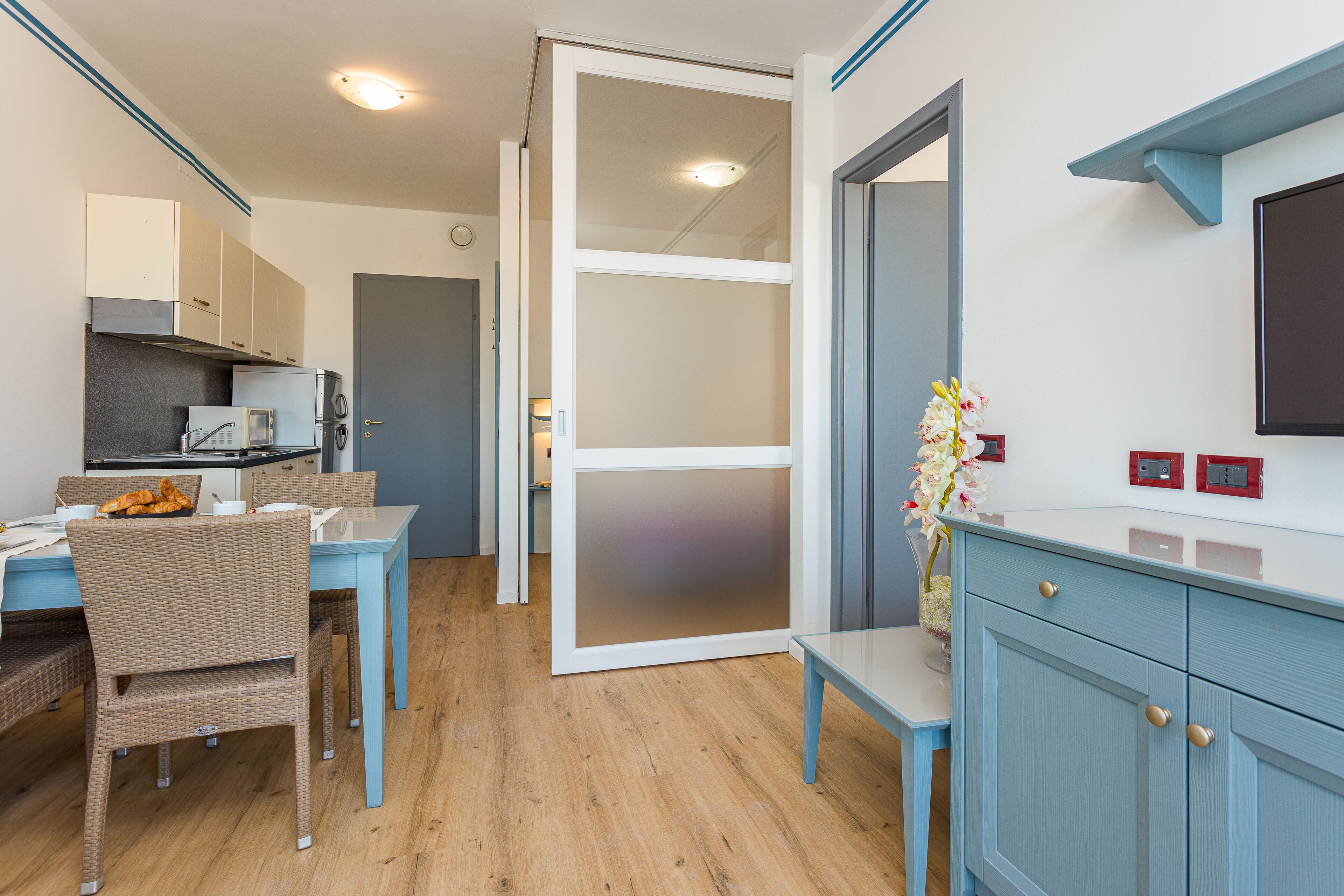 A modern kitchen with a dining area, wooden flooring, and light blue cabinetry.