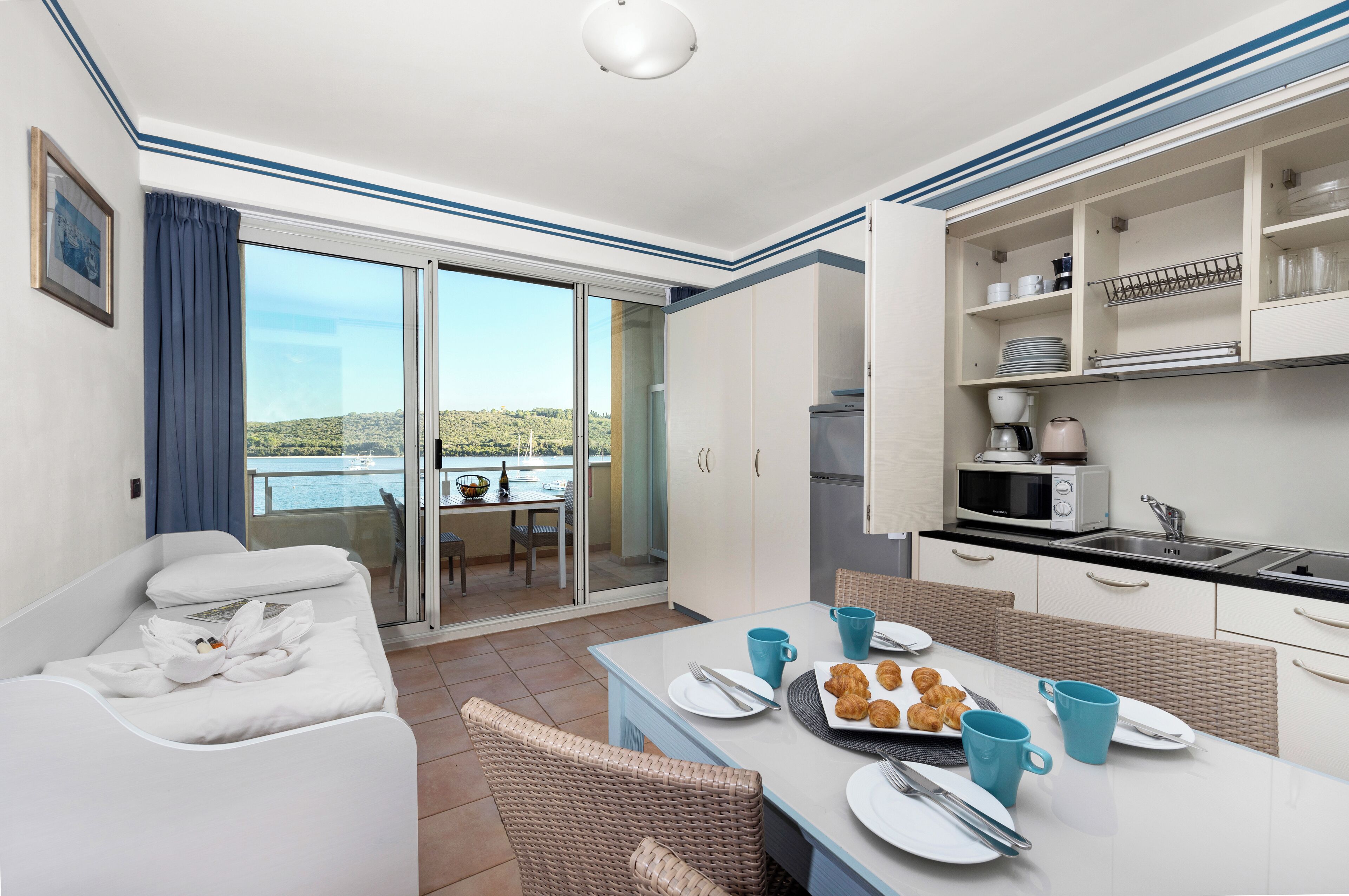 Une chambre d’hôtel avec balcon, un coin repas où le petit-déjeuner est servi, et une kitchenette.