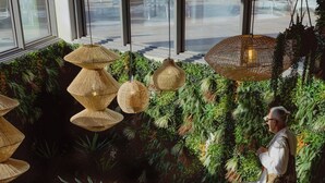 Un interior moderno con lámparas de mimbre colgantes, exuberantes jardines verticales verdes y una persona caminando.